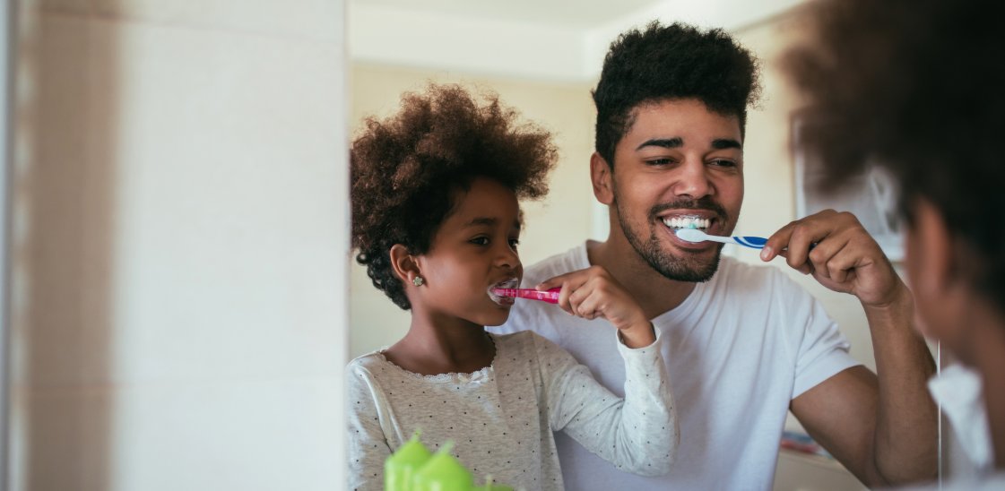 Man and young girl brushing their teeth in the mirror