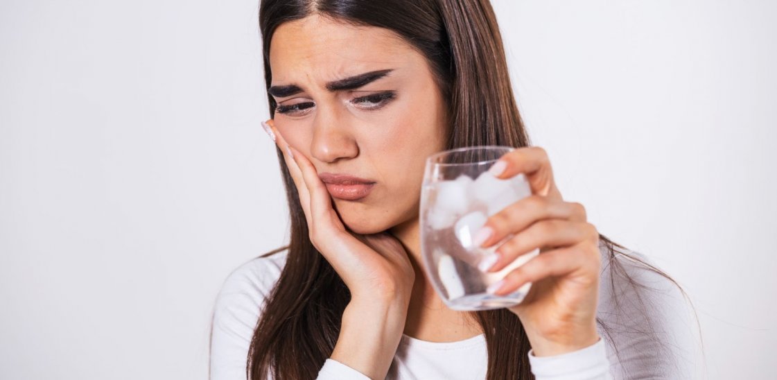 Young woman with sensitive teeth holding a glass of cold water with ice