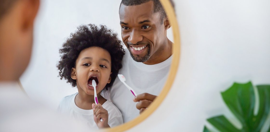 Image alt text: a father and son brushing teeth together in the bathroom.