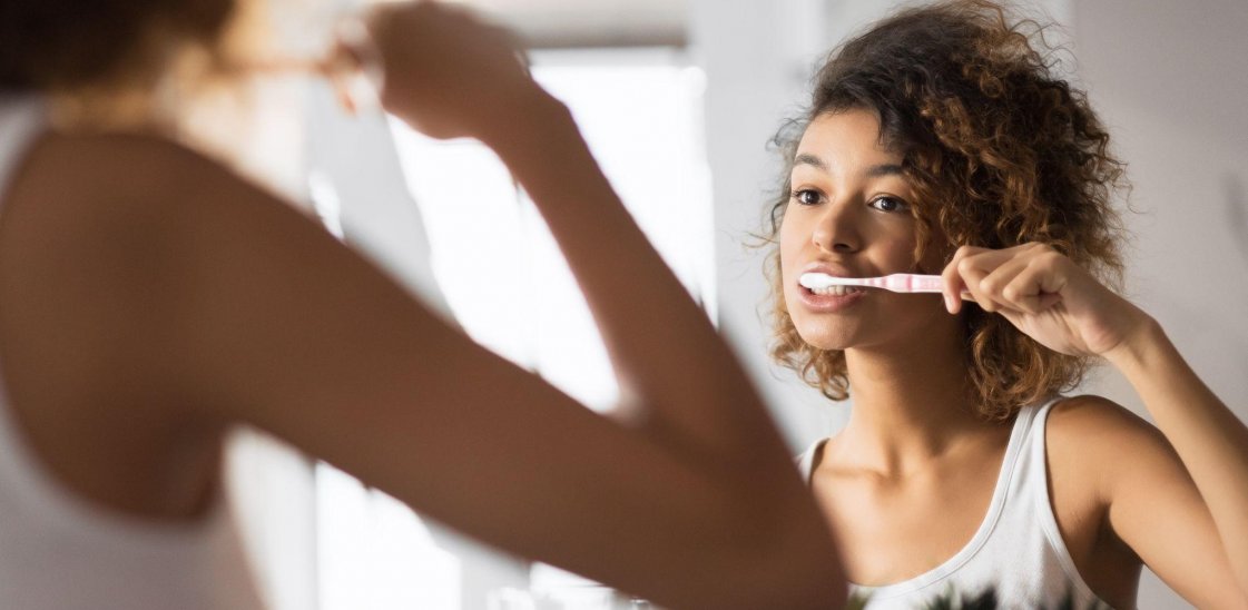 woman brushing teeth while looking in bathroom mirror