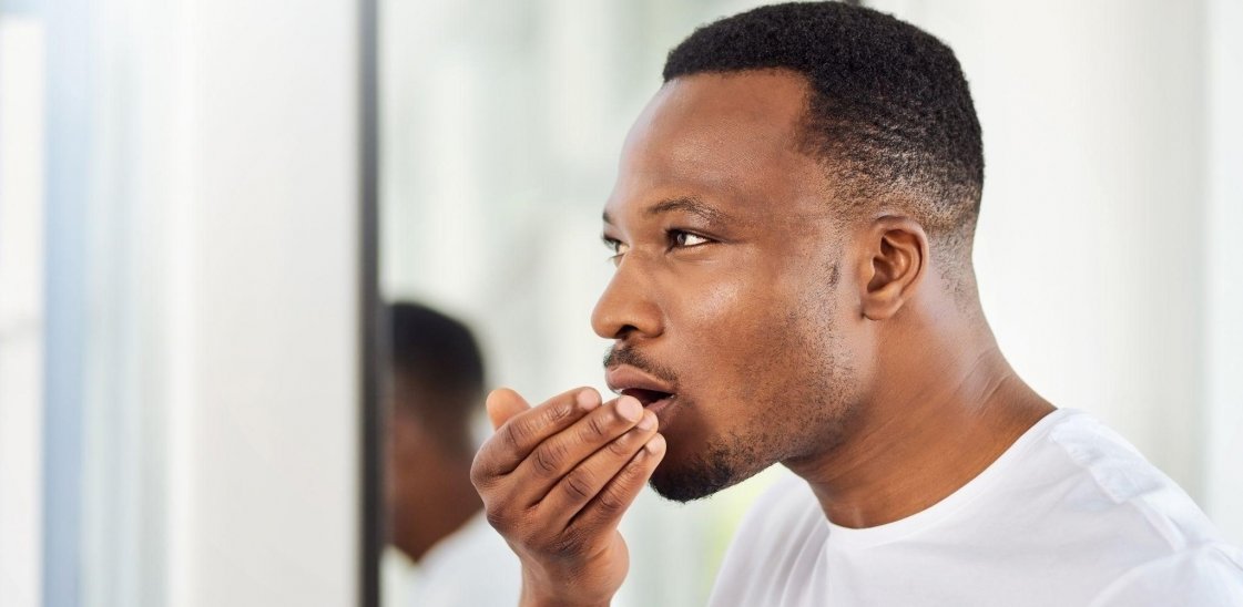 young man smelling his own breath during his morning grooming routine