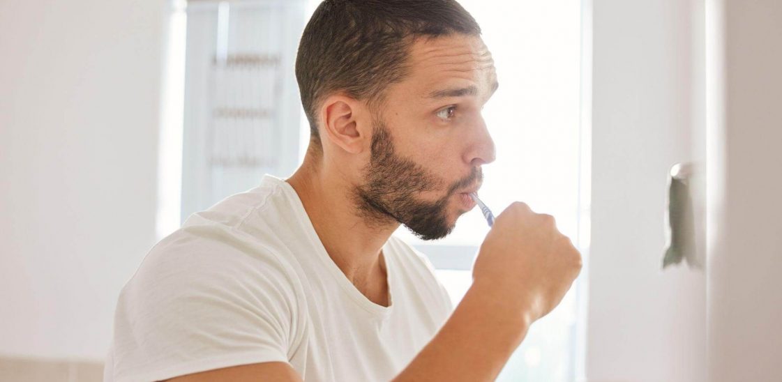 A man brushing his teeth while looking in the mirror