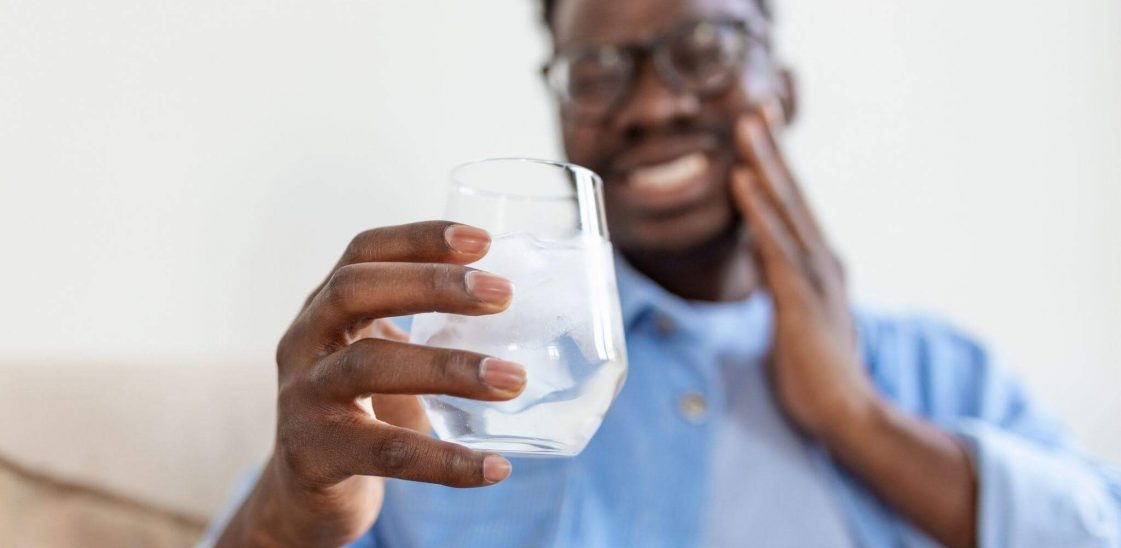 A young man with sensitive teeth holding a glass of ice water