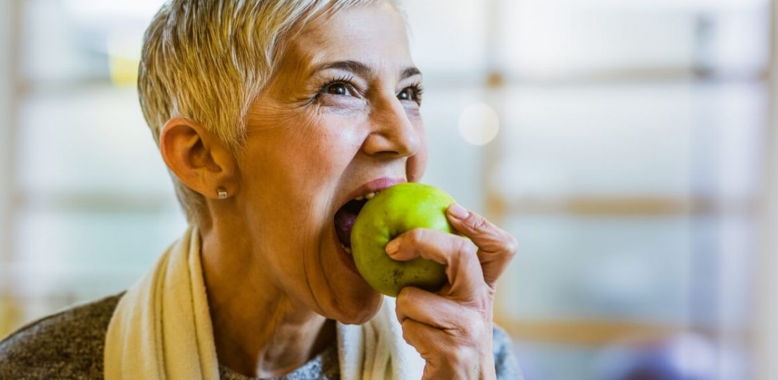 An elderly woman bites into an apple