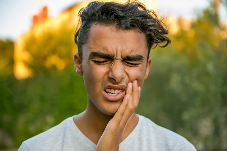 A young man holds his jaw in pain from a tooth abscess.