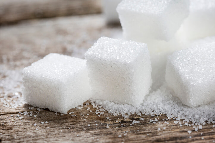 A pile of white sugar cubes and granules on a wooden table top