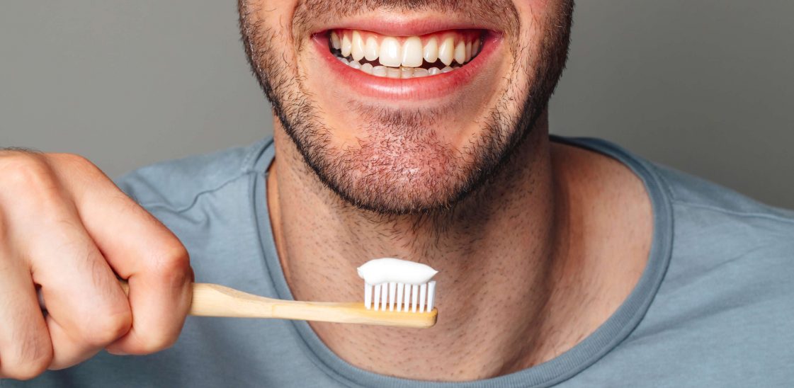 Man with white and health teeth smiling, holding a toothbrush in his hand