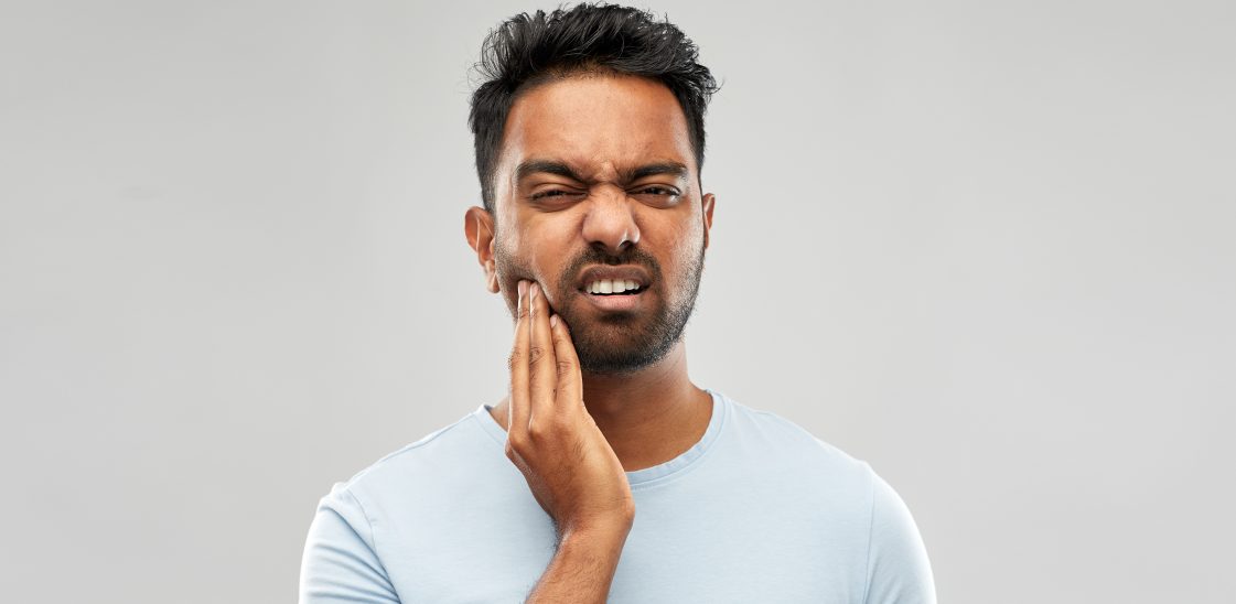 A man holds his face, experiencing temporomandibular joint jaw pain