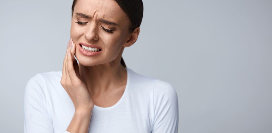A woman holds the right side of her jaw in pain.