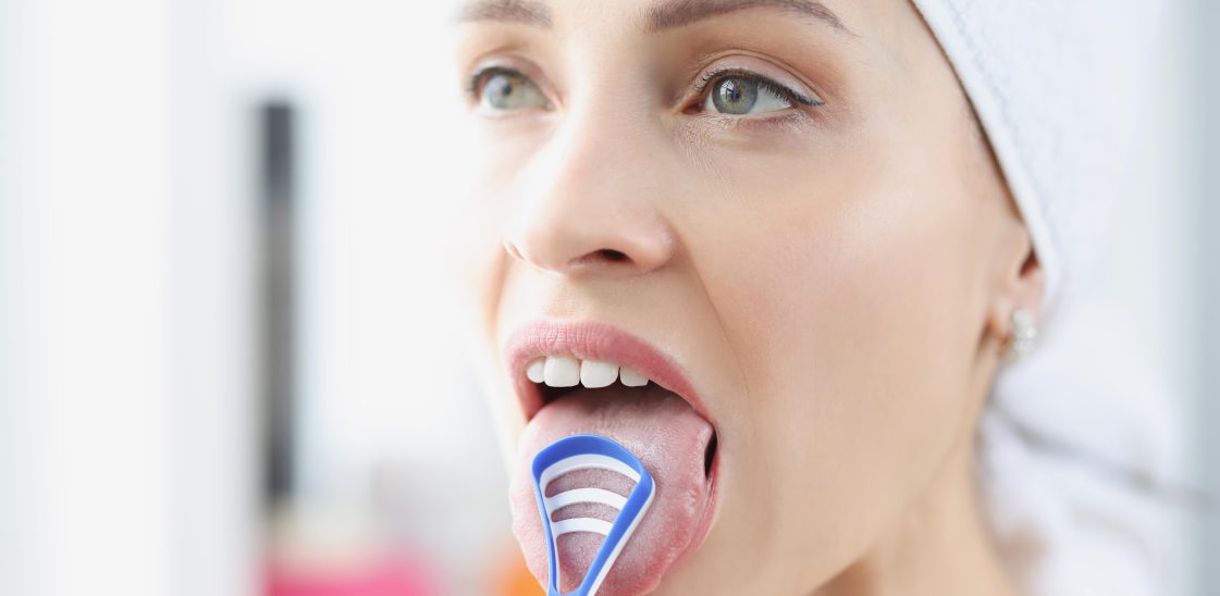 A woman uses a tongue scraper to clean her tongue.
