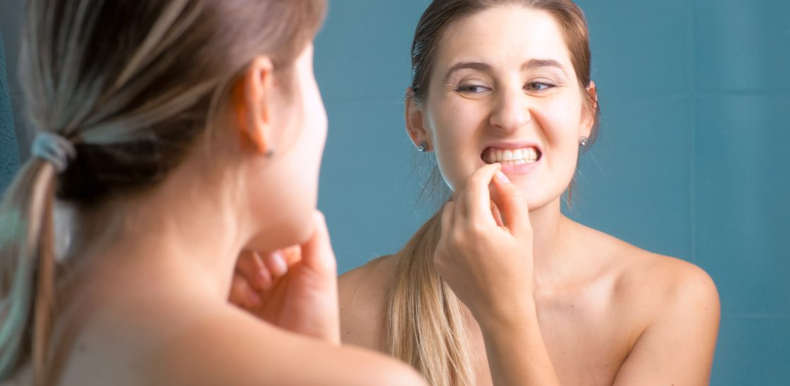 A woman using a mirror while trying to dislodge food stuck between her teeth