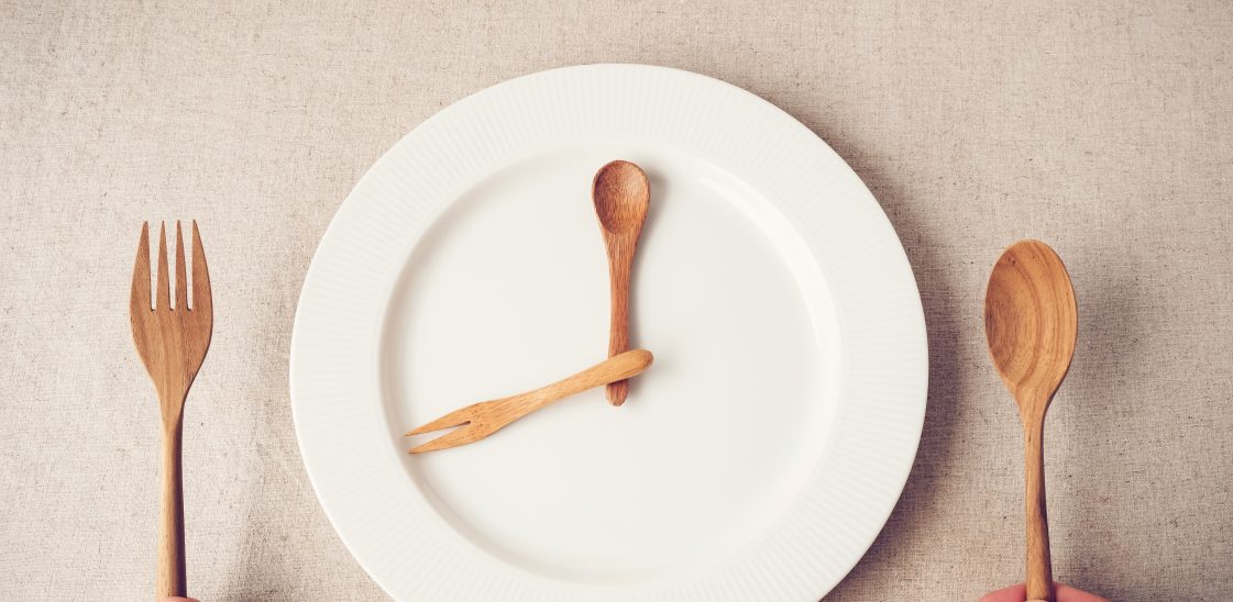 empty white plate with wooden spoon and fork representing hands on a clock