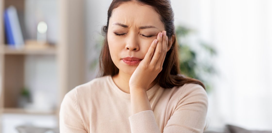 young woman grimacing with hand to face due to dental pain