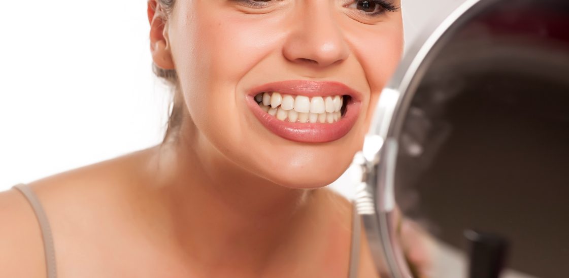 Young woman looking her teeth on the mirror