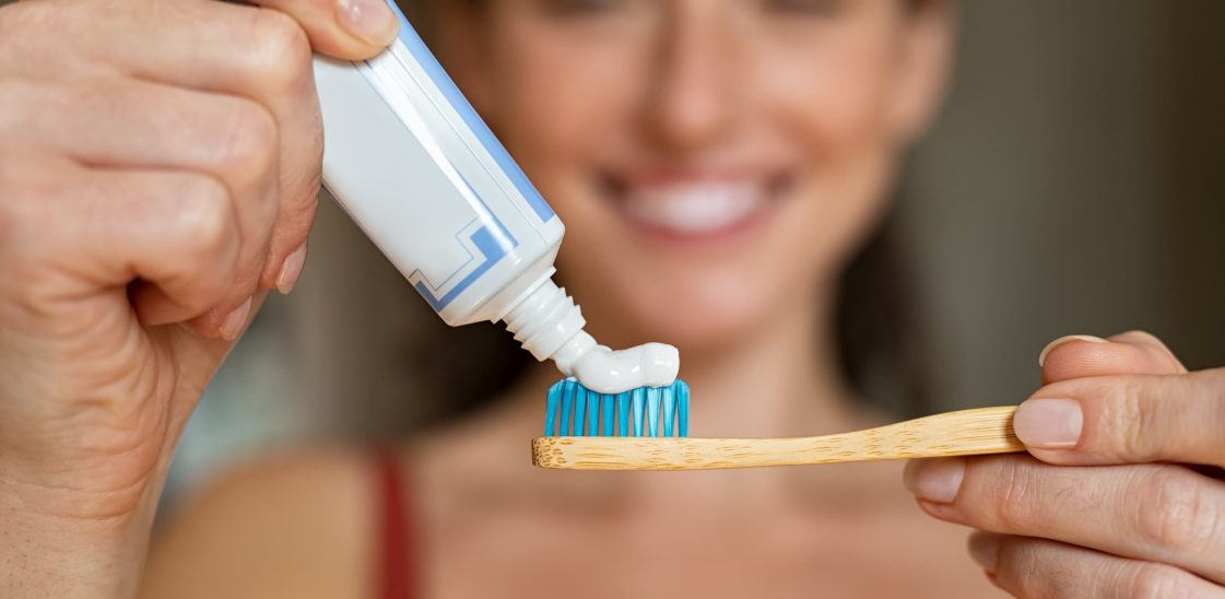 A woman applies toothpaste to a bamboo toothbrush.