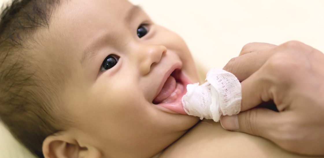 A parent uses gauze wrapped around their finger to clean their baby’s mouth.