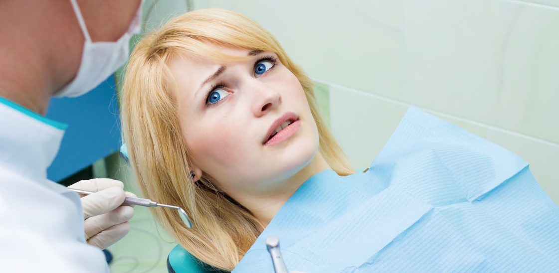 A young woman having dental treatment looks up at her dentist anxiously.
