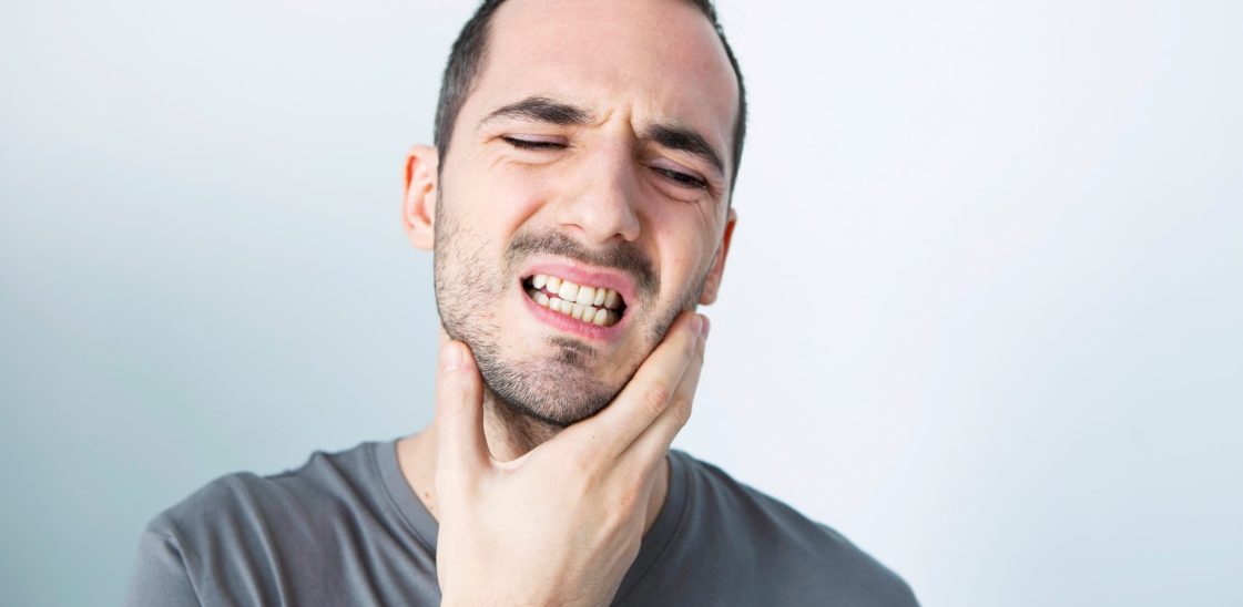 A man holds his jaw, in pain from bruxism or teeth grinding.