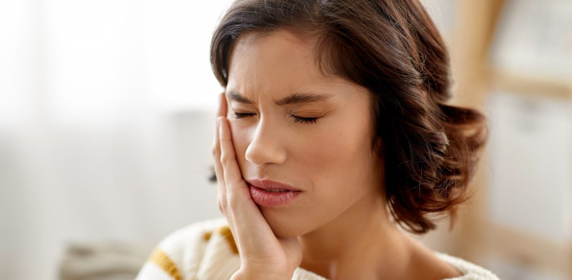 A woman holds her jaw, in pain from a toothache.