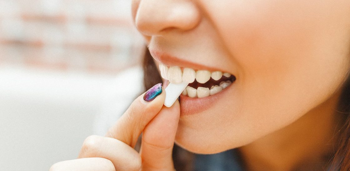 A close-up of a woman putting a piece of gum between her teeth.