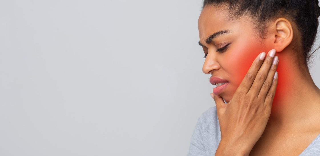 A woman with a pained expression holds her hand to her face.