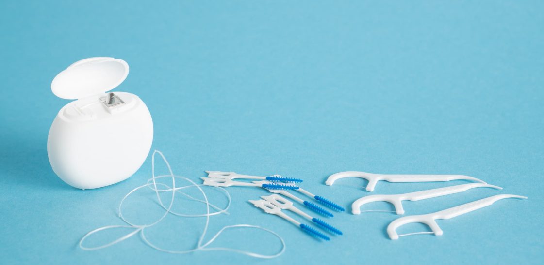 Rolled dental floss, interdental picks and floss picks against a blue background.