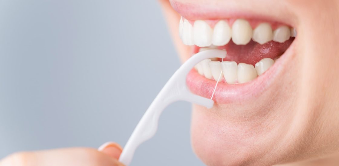 A woman uses a dental floss pick to clean between her teeth.